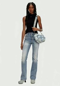 Svart ärmlös topp, ljusblå flarejeans med slitna detaljer, grå axelväska och grå plattformsskor. Enhetlig bakgrund.