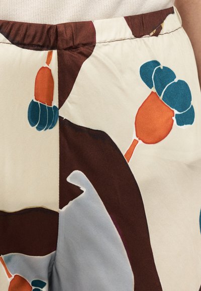 Blomstrete mønstret stoff med farger i krem, blågrønn, oransje og brun; glatt tekstur; elastisk midje; nærbilde som viser designdetaljer.