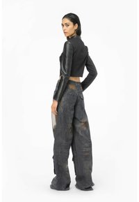 Chaqueta de cuero negra recortada con mangas largas, combinada con pantalones de mezclilla oscuros de corte holgado que presentan grandes desgastes y un acabado desgastado.