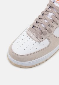 Beige suède en witte leren sneaker met perforaties, platte veters en rubberen zool. Beschikt over een klein wit logo aan de zijkant.