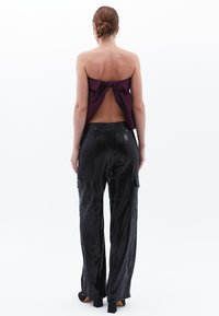 Paarse strapless top met een knoop op de rug, gecombineerd met hooggeknoopte zwarte glitter cargo pants met zijzakken en een relaxte pasvorm.