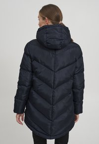 Marineblauer gepolsterter Parka mit Kapuze, der ein diagonales Steppmuster aufweist, lange Ärmel und einen abgerundeten Saum hat. Glatte, glänzende Textur.
