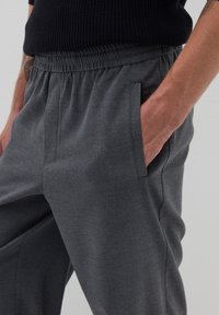 Graue elastische Hose mit seitlichen Taschen, die eine glatte Textur und eine taillierte Passform aufweist und ein dezent strukturiertes Stoffmuster betont.
