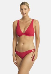 Rode bikini set met een diepe halslijn top met brede banden en een bijpassende bikinibroek met verstelbare strikken en uitsparingen aan de zijkanten. Glad textuur.