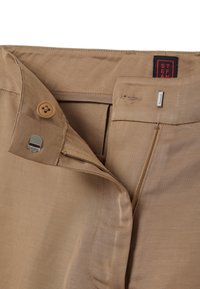 Beige Hose aus glattem Stoff mit einem Knopfverschluss und einem Reißverschluss. Mit einem kleinen metallischen Akzent in der Nähe des Bundes.