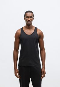 Maiou negru din bumbac, cu decolteu rotunjit și bretele late. Prezintă un mic logo brodat pe piept.