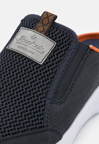 Scarpa slip-on con tomaia in rete blu navy, superficie testurizzata e un'etichetta grigia. Presenta un accento arancione e una suola bianca per contrasto.