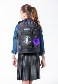 Zaino nero con motivo a ragnatela, strisce viola, logo a scudo e un portachiavi con pompon viola; manici resistenti e tessuto strutturato.