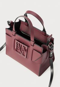 Sac à main en cuir bordeaux avec poignées supérieures et une bandoulière amovible. Dispose d'un logo embossé à l'avant, d'une fermeture éclair et de poches intérieures.