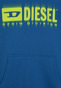 Felpa blu con cappuccio caratterizzata da una grande grafica gialla sfumata con il testo "DIESEL DENIM DIVISION." Include una tasca frontale e una consistenza morbida.