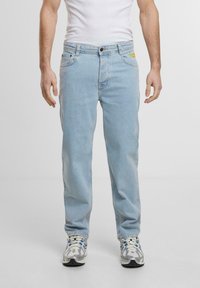 Heledad denim teksad helesin, sirgedalt lõigatud jalad, viie tasku disain ja diskreetne kollane logo parema tasku kohal.