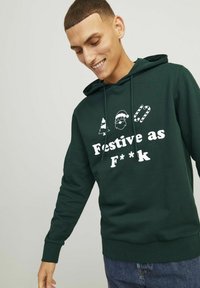 Felpa verde scuro con stampa bianca di motivi festivi (albero, Babbo Natale, bastoncino di zucchero) e testo "Festivo come un C**zo." Cappuccio regolabile e polsini a coste.