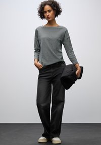 Grå långärmad topp med båtutskärning, i kombination med svarta vida jeans och beige sneakers; håller en svart pufferjacka.