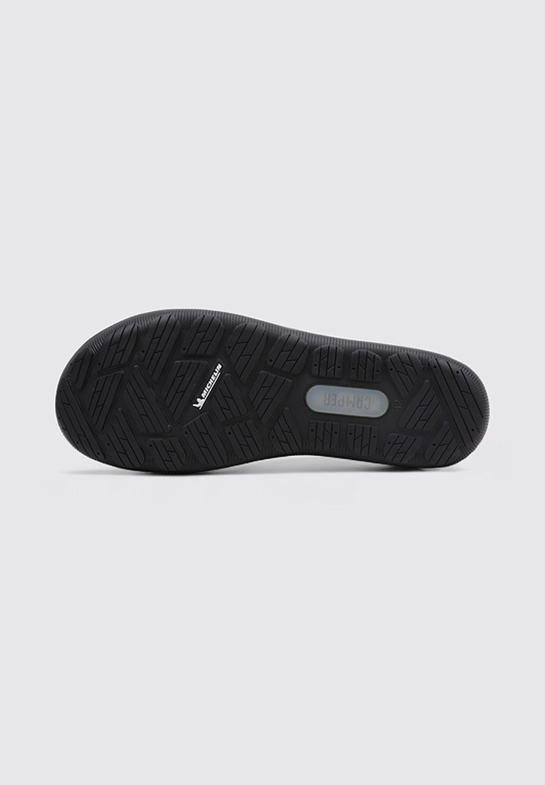 Black rubber shoe sole with a textured, patterned surface for traction. Features a central logo and varies in tread design.