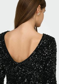 Vestido negro con lentejuelas y escote en V profundo en la espalda. La textura es brillante y reflectante, resaltando los intrincados detalles de las lentejuelas.
