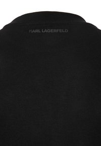 Suéter negro con textura acanalada y cuello redondo. Presenta una etiqueta sutil impresa "KARL LAGERFELD" en la parte posterior.