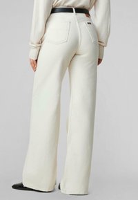 Pantalones de pierna ancha en tejido color crema, con cintura alta, bolsillos traseros y un cinturón negro en contraste. Textura suave.