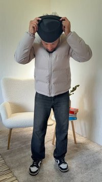 Μπουφάν puffer σε ανοιχτό γκρι με φερμουάρ μπροστά και πλαϊνές τσέπες, συνδυασμένο με σκούρο τζιν και μαύρα sneakers. Υφή φόντου και καρέκλα.