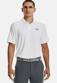 Hvid poloshirt med krave, forsynet med et lille gråt Under Armour-logo. Båret med grå bukser og et gråstribet bælte. Glat stofoverflade.