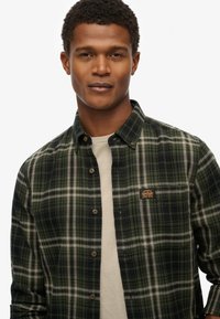 Groene en marineblauwe geruite button-up shirt met een beige onderhemd, voorzien van een logopatch en bruine knopen, gemaakt van textuur katoen.