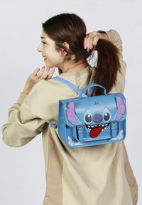 Mochila de cuero azul con un diseño del personaje Stitch, que presenta orejas grandes, una cara impresa y acentos florales en la parte inferior.