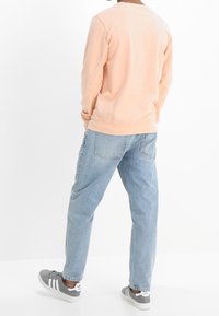 Jasnoróżowa bluza z ribbowanymi mankietami, w połączeniu z jasnoniebieskimi dżinsami. Szare sneakersy z białymi paskami dopełniają zestaw.