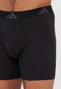 Boxer briefs pretos feitos de material elástico, com uma ampla cintura elástica apresentando um padrão de logótipos cinzentos e costura reforçada.