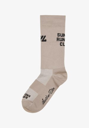 Chaussette de sport beige avec le texte noir "Sunset Run Club", présentant un orteil renforcé, un design de panneaux contrastés et une texture lisse.