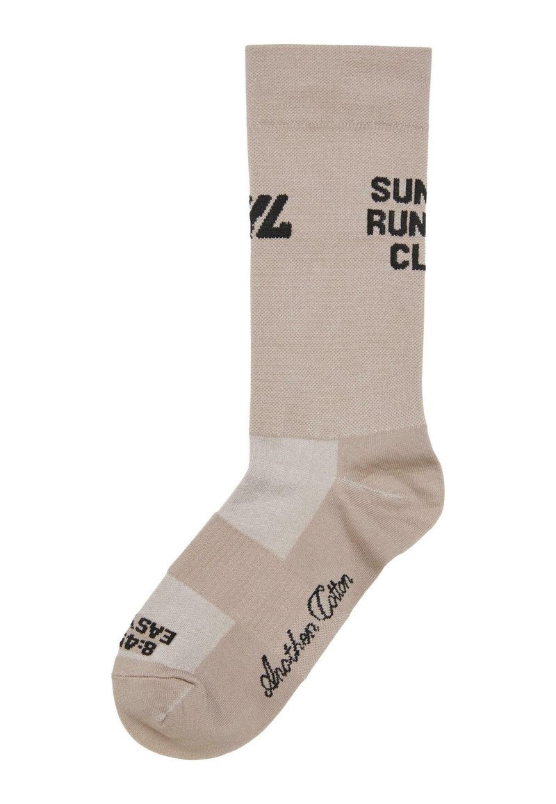Calza sportiva beige con testo nero "Sunset Run Club", dotata di punta rinforzata, design a pannelli contrastanti e texture liscia.