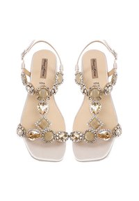 Sandali piatti beige con accenti decorativi di cristallo, dotati di un design a T, una texture liscia e punte quadrate. Finitura leggermente lucida.