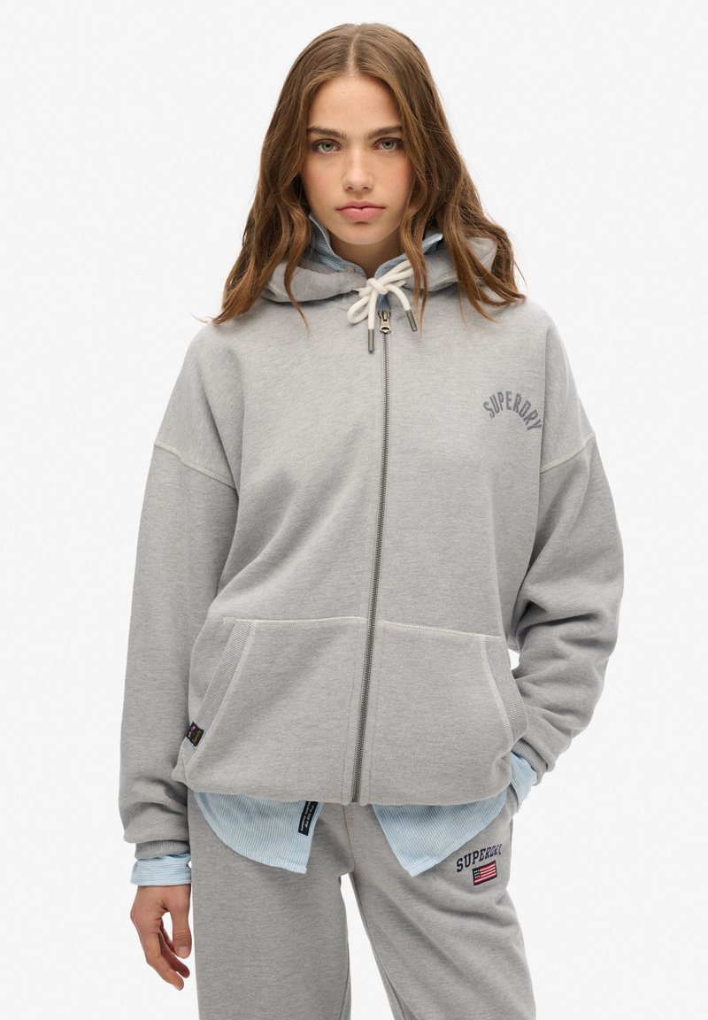 Graue Zip-Hoodie aus weicher Baumwolle, mit geräumiger Passform, zwei Fronttaschen und einem gestickten Logo auf der Brust. Kapuze mit Kordelzug.