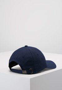 Granatowa czapka baseballowa z bawełny, z wygiętą daszkiem, regulowanym paskiem i haftowanym logo z tyłu. Gładka tekstura.