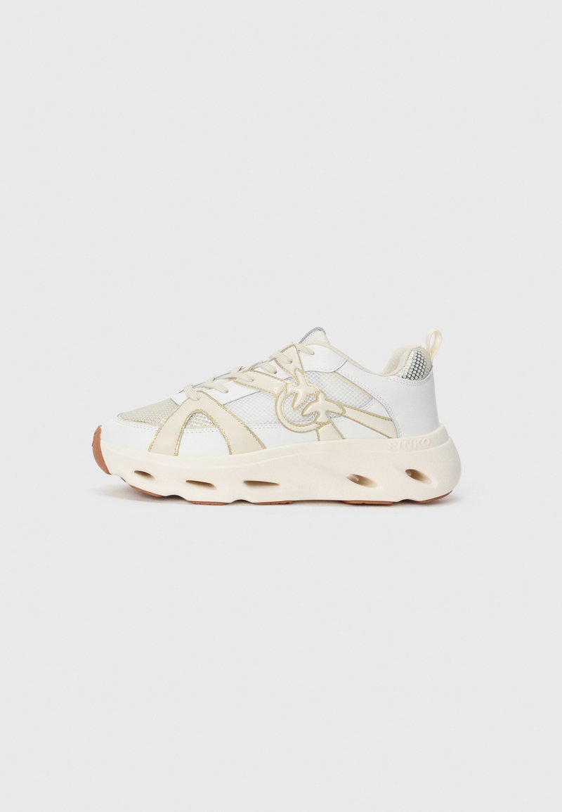 White athletic sneaker with a textured upper, beige accents, a thick sole featuring cutouts, and a reflective detail on the heel.