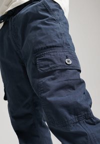 Pantalones cargo de color navy hechos de una tela ligera, que cuentan con un bolsillo lateral con cierre de botón y detalles de costura visibles.