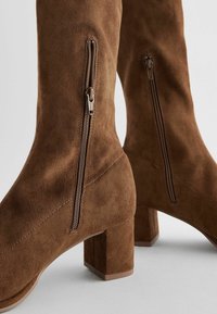 Stivali al ginocchio in suede marrone con tacco a blocco, doppi zip laterali e dettagli di cucitura in vista, offrono un aspetto testurizzato.