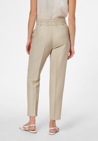 Beige skräddarsydda byxor med vertikala randiga mönster, sidofickor och en åtsittande midja med distinkt accentuerande hårdvara vid midjebandet.