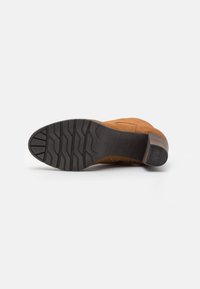 Bottine en daim brun avec une semelle en caoutchouc noir texturé. Présente un bout rond et un minimum de couture sur le côté.