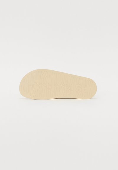 Beige sko sål med tekstureret overflade, der har et bølget mønster og brandlogo præget. Kanten er let afrundet.