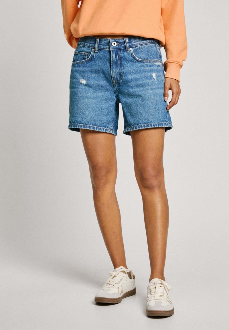 Bermudas de denim en un azul claro con detalles desgastados, de corte recto y con dobladillos enrollados, combinadas con zapatillas blancas.