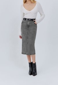 Gonna midi in denim grigio con tasche, vestibilità dritta e una cucitura frontale. Abbinata a un top bianco a coste e stivali neri alla caviglia.