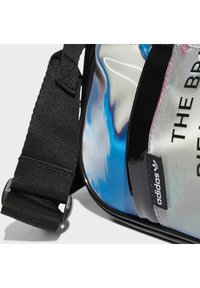 Czarny pasek na kolorowej, błyszczącej torbie z niebieskimi i białymi abstrakcyjnymi wzorami. Etykieta marki widoczna z boku.