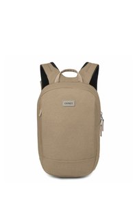 Sac à dos en tissu beige avec une forme rectangulaire, doté de bretelles rembourrées, d'une poignée supérieure et d'une poche zippée à l'avant. Étiquette de marque visible.