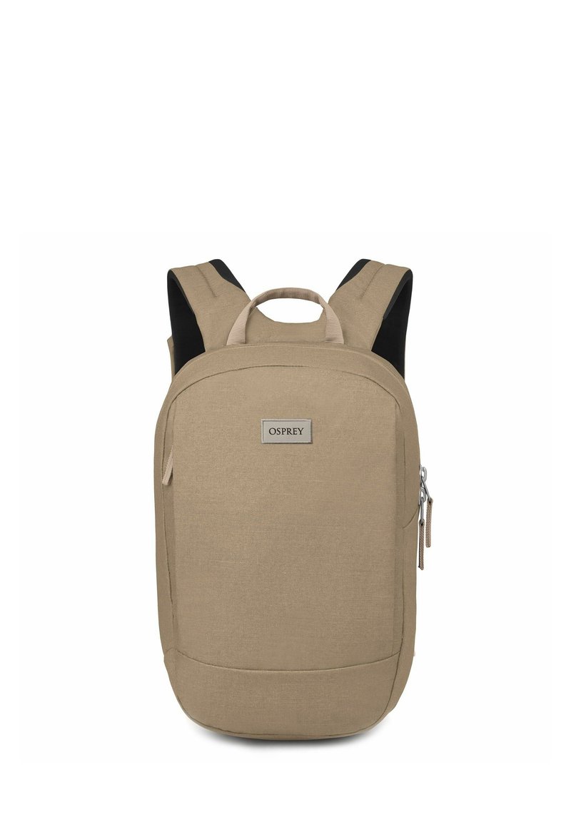 Sac à dos en tissu beige avec une forme rectangulaire, doté de bretelles rembourrées, d'une poignée supérieure et d'une poche zippée à l'avant. Étiquette de marque visible.