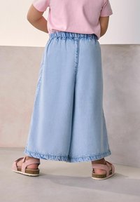 Világoskék, bőszárú farmer culotte, rugalmas derékkal, rózsaszín szandálokkal párosítva. Az alja nyers szélekkel van kialakítva.