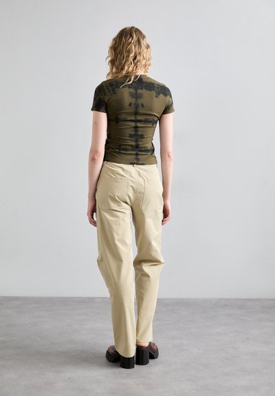 Olive green tie-dye short-sleeve shirt paired with light beige loose-fitting trousers and chunky black platform shoes. Smooth fabric texture.