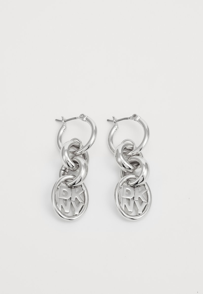 Silver hoop earrings featuring intertwined chains and circular charms with "DKNY" lettering. High-shine metal finish with smooth texture.