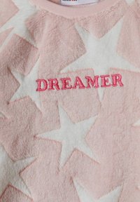 Sweatshirt en polaire rose avec des motifs d'étoiles, portant l'inscription "DREAMER" brodée en fil rose. Texture douce et col rond.