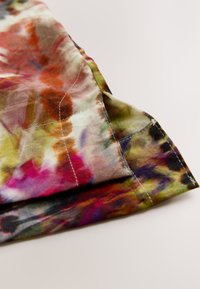 Farebná, ľahká látka s batikovaným vzorom v zelených, oranžových a fialových odtieňoch. Na okrajoch je viditeľné prešívanie.