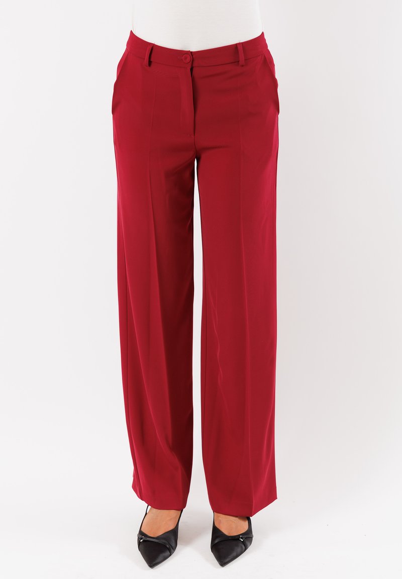 Pantaloni larghi rossi con una texture liscia, dotati di una vita piatta e chiusura a bottone. Abbinati a scarpe nere a punta.