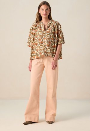 Blouse à motifs floraux dans des tons terreux associée à un pantalon évasé rose pâle. La blouse présente un col en V et des manches courtes, tandis que le pantalon est à jambes larges.
